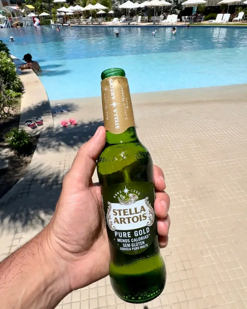 Japaratinga Resort All Inclusive, segurando cerveja sem glúten em frente a piscina